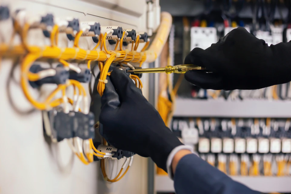 Technicien en combinaison travaillant sur panneau &eacute;lectrique industriel, manipulation de c&acirc;bles avec outil de pr&eacute;cision
