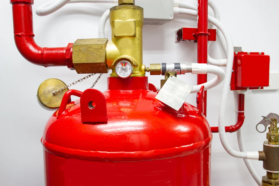 Installation de protection incendie en intérieur avec réservoir rouge sous pression, manomètre de contrôle, raccords laiton, tuyauterie rouge et flexible blanc
