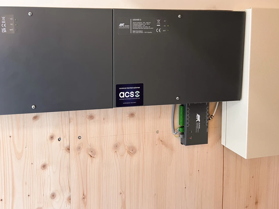 Technicien en tenue professionnelle installant ou vérifiant un système de contrôle d'accès moderne sur un mur - panneau de commande à clavier, lecteur de badge ou biométrique - montrant des mains effectuant l'installation ou la configuration de l'équipement, dans un environnement intérieur professionnel (immeuble, bureau ou copropriété).