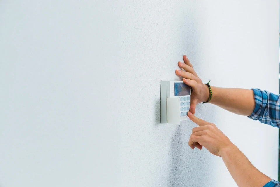 Homme installant un système de sécurité mural intérieur, programmant un boîtier de contrôle d'accès électronique avec clavier numérique et écran LCD