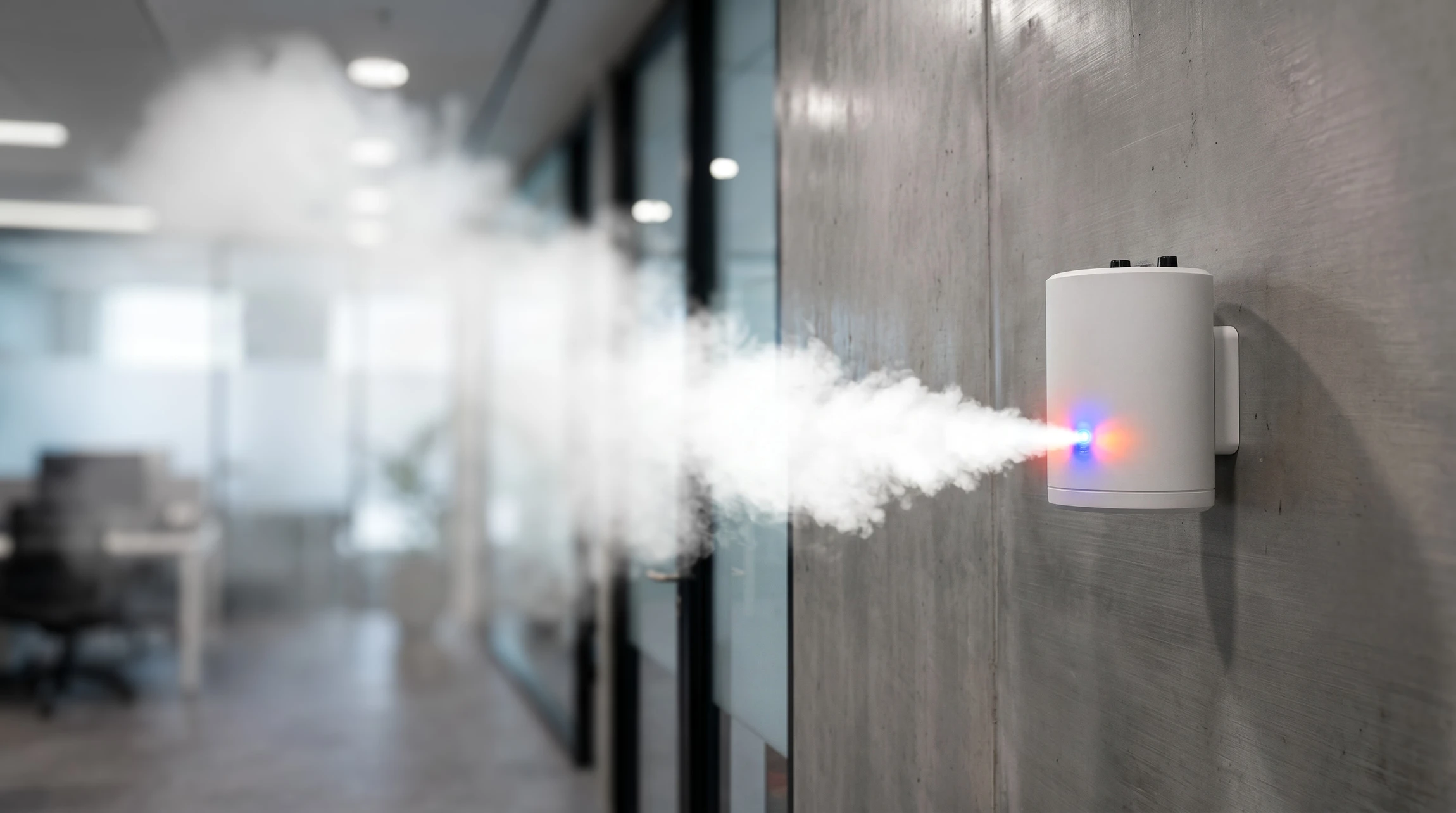 Photographie professionnelle d'intérieur d'un bâtiment commercial ou résidentiel haut de gamme montrant un générateur de brouillard anti-intrusion activé, créant une brume dense qui remplit progressivement l'espace. La scène doit montrer l'efficacité du système : le brouillard opaque masquant complètement la visibilité de l'intérieur depuis l'extérieur, avec des éléments architecturaux distinctifs (vitres, portes, murs) légèrement visibles à travers la brume. Éclairage naturel et ambiant pour souligner le contraste entre l'intérieur brumisé et l'espace dégagé. L'image doit dégager une impression de sécurité professionnelle et de protection efficace.