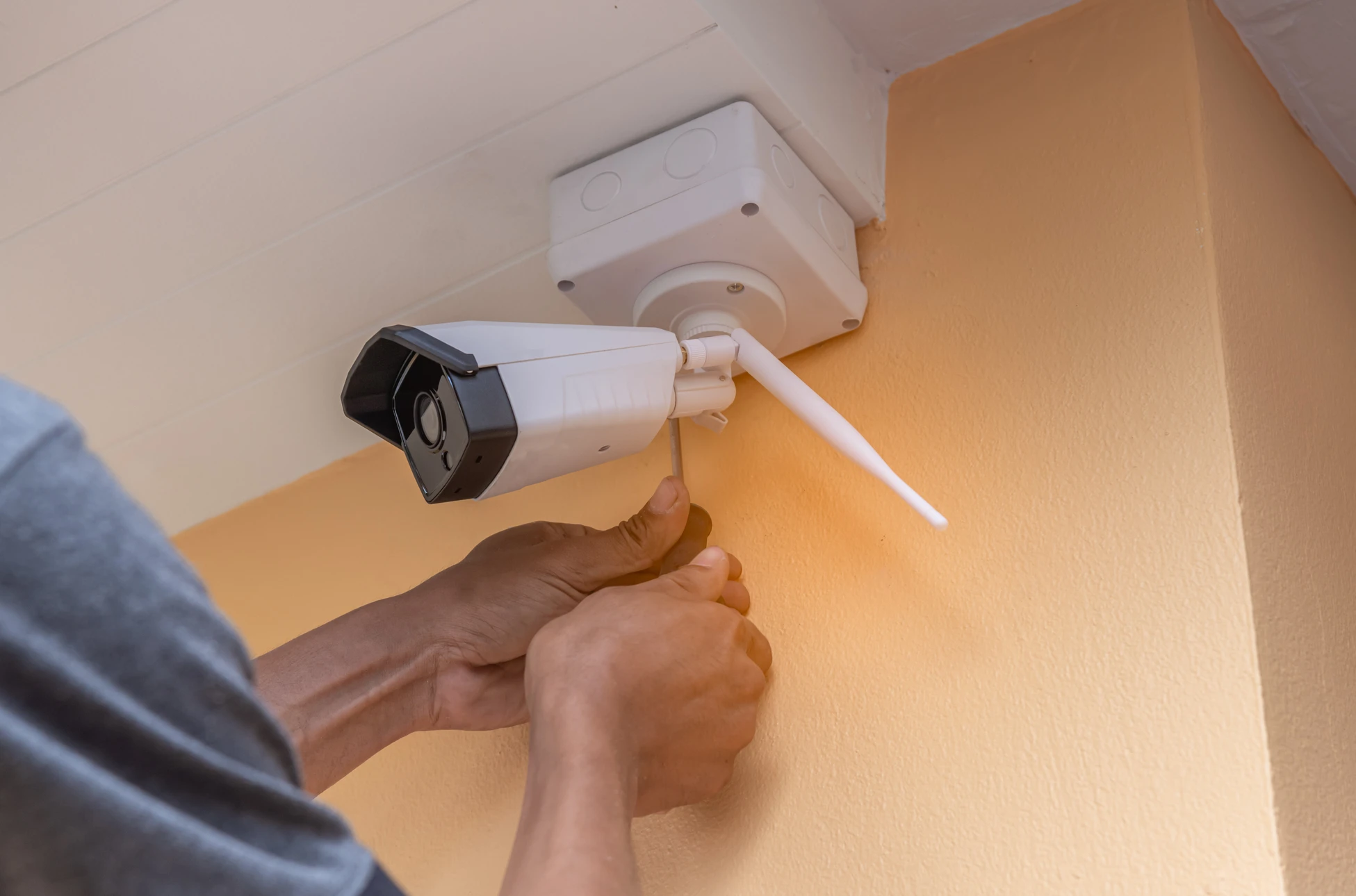Un homme en chemise à carreaux bleus installe ou configure un panneau de commande d'alarme de sécurité domestique sur un mur blanc intérieur