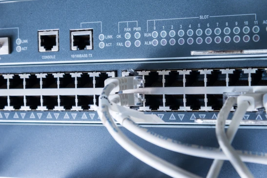 Int&eacute;rieur de datacenter avec technicienne en chemise bleue utilisant une tablette tactile pour surveiller les &eacute;quipements r&eacute;seau