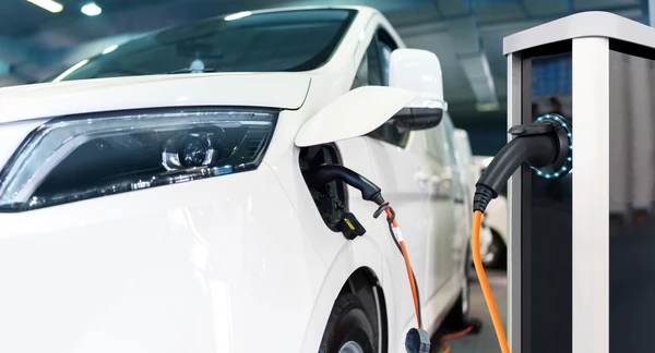 Sc&egrave;ne ext&eacute;rieure urbaine avec v&eacute;hicule &eacute;lectrique blanc en charge sur borne publique