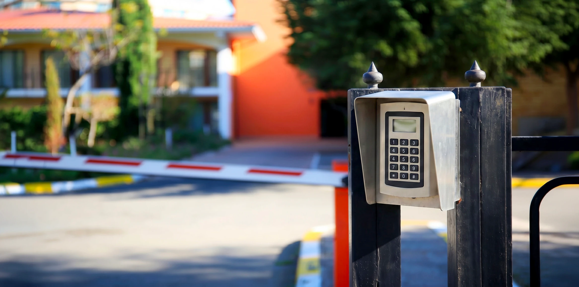 Photographie professionnelle en gros plan d'une main appuyant sur un bouton ou une touche d'un système d'interphonie/contrôle d'accès moderne installé en façade ou à l'entrée d'un bâtiment. Le système doit être de qualité professionnelle, avec design épuré et discret. L'arrière-plan montre légèrement une porte d'entrée moderne ou une façade classe. L'éclairage est professionnel et met en valeur le dispositif de sécurité. La scène traduit la sécurité, l'accessibilité et le professionnalisme.