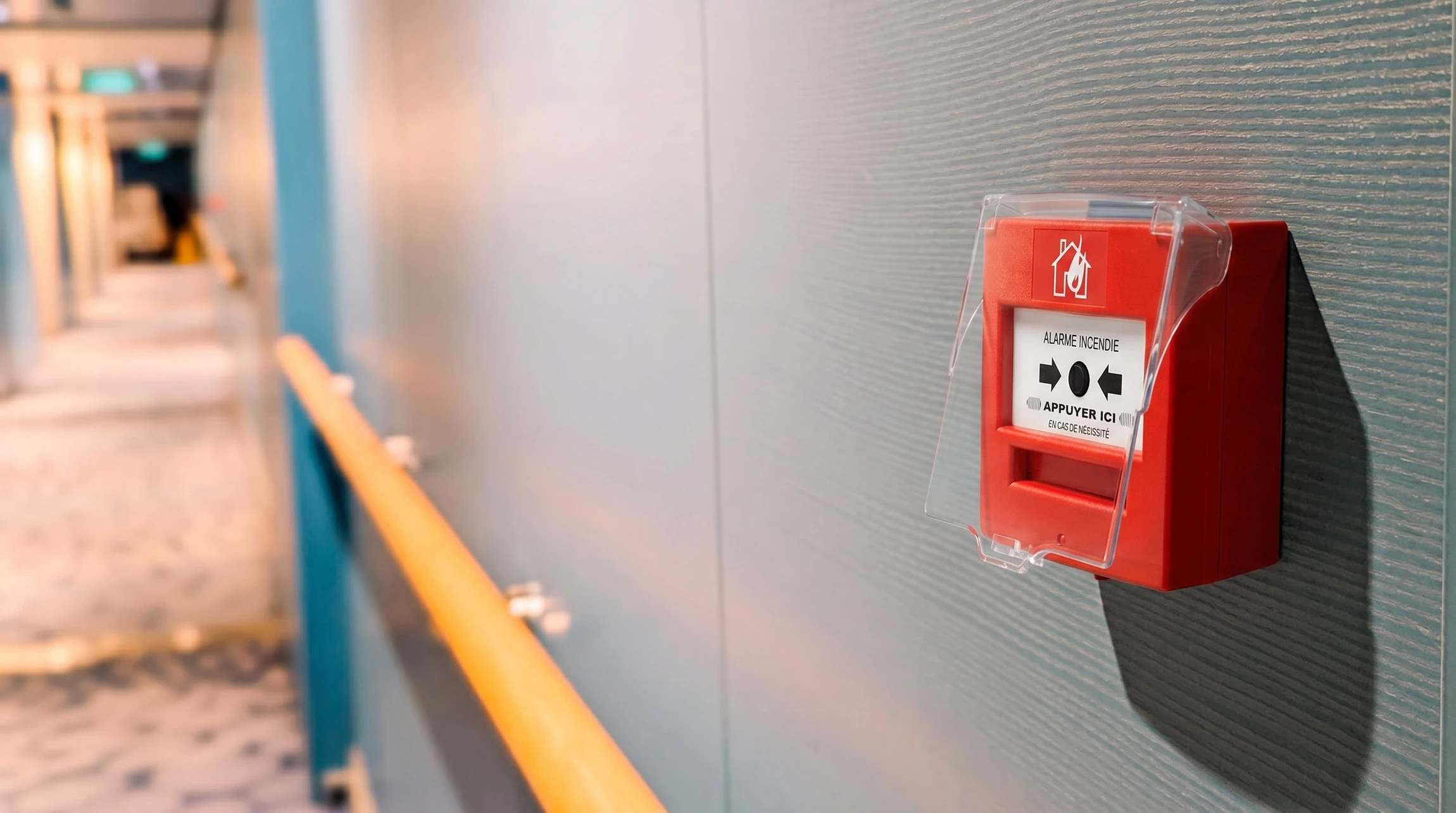 Intérieur d'un bâtiment avec mur blanc où est fixé un déclencheur manuel d'alarme incendie rouge