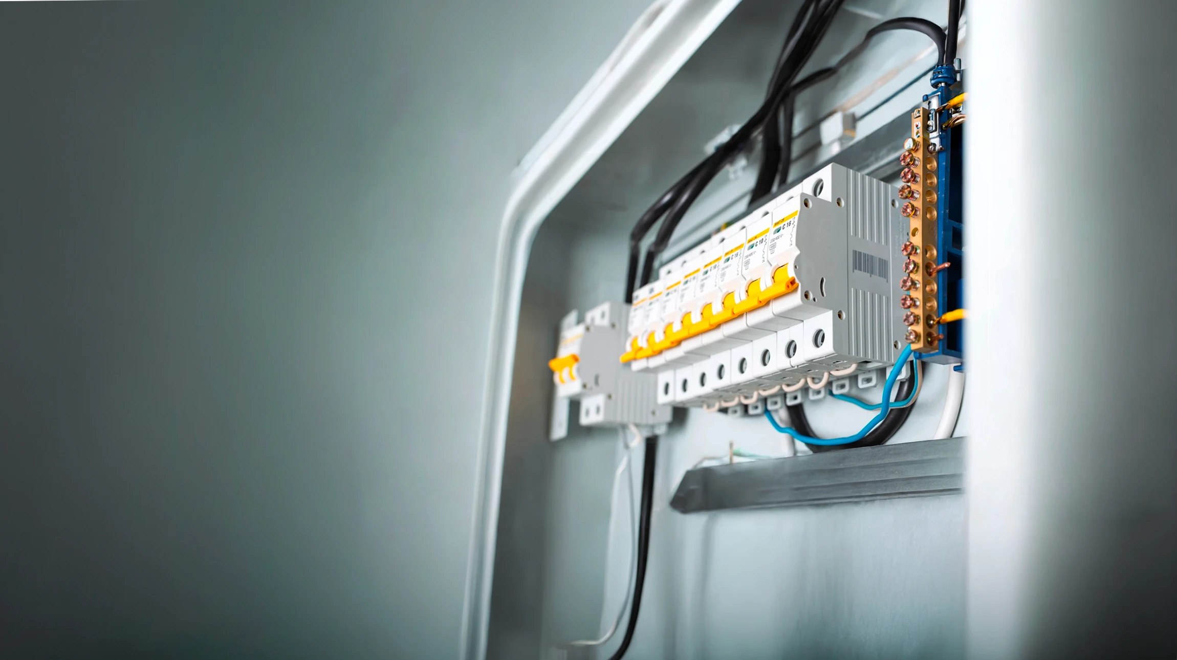 Un électricien en chemise à carreaux et gants de protection travaille sur un tableau électrique dans un local technique